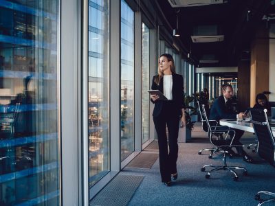 Woman in office looking out window with people in the bckground